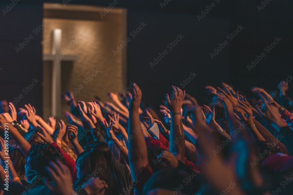 Fototapeta premium Christian crowd raising hands in worship towards cross during church service