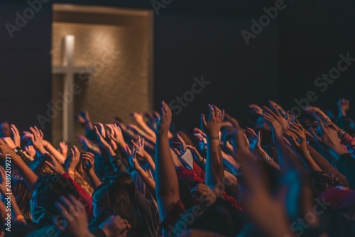 Christian crowd raising hands in worship towards cross during church service
