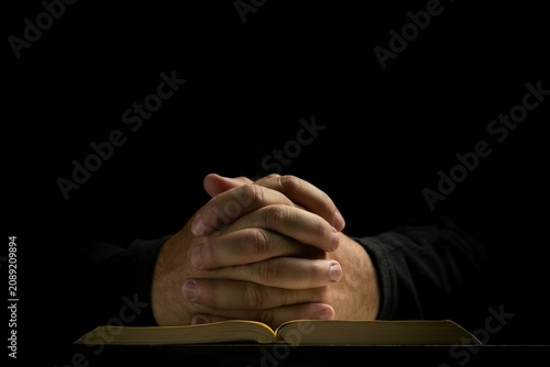 Obraz na płótnie Devout believer praying with folded hands over holy bible in complete darkness
