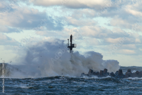 Photos Waves crashing at breakwater with beacon under cloudy sky