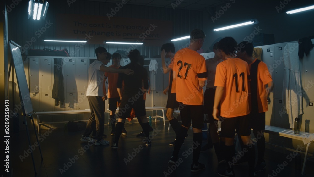 Fototapeta premium Group of Diverse Teenage Boys in Orange Uniforms and Coach Celebrate Win in Locker Room. Male Players Jumping, Shouting, and Hugging. Concept of Pure Euphoria and Emotional Success of Youth Sports.