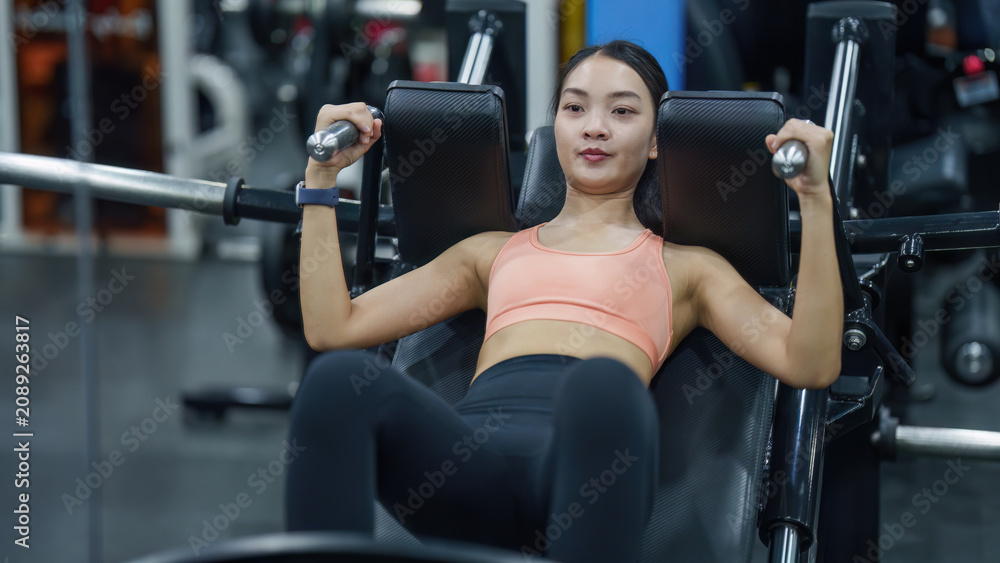 Fototapeta premium Asian woman using hack squat machine in gym for leg strength workout