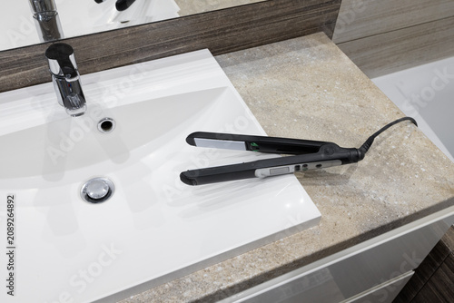 hair straightener on white bathroom sink showing beauty routine and personal care concept, hygiene and wellness lifestyle