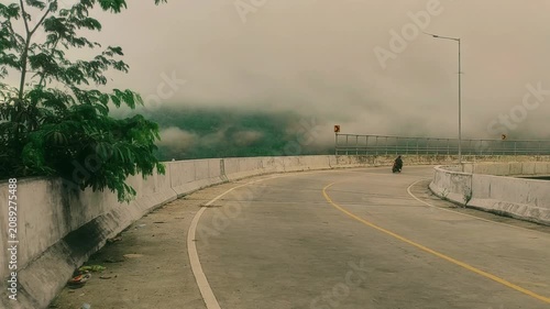 A winding road disappears into thick, atmospheric mist blanketing distant mountains, creating a serene and solitary journey through a mystical, fog-laden landscape