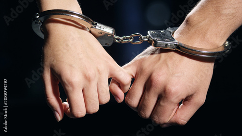 Bild auf Leinwand Close-up of a young woman's and a man's hands with wrists bound by chrome steel handcuffs tenderly holding each other by interlocked pinky fingers