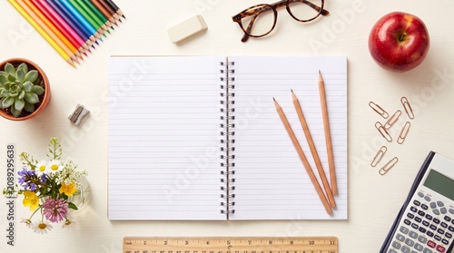 Blank spiral notebook on white desk with school supplies, creative workspace with colorful pencils and red apple, student stationery flat lay