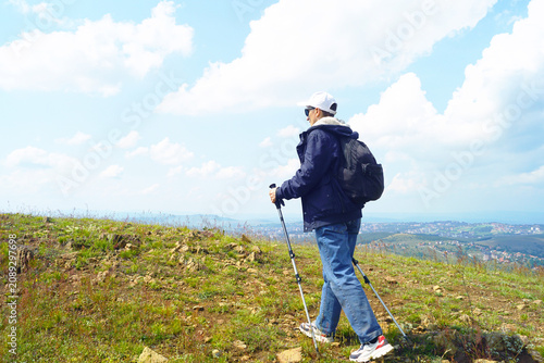 Slika na platnu Traveler with backpack and poles crossing upland plateau overlooking city in valley below