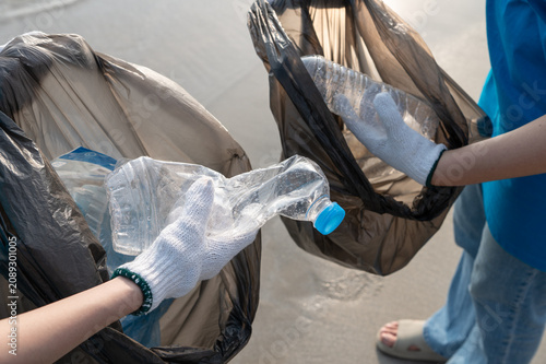 Two volunteers are collecting plastic bottles and putting them in a trash bag on the beach. They are enjoying doing this environmental activity together.