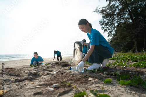 Group of active Asian volunteers cleaning up plastic waste and garbage on the beach together, focusing on environmental conservation and community teamwork.