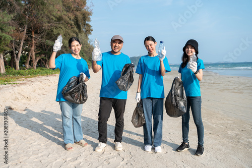 Group of active Asian volunteers cleaning up plastic waste and garbage on the beach together, focusing on environmental conservation and community teamwork.