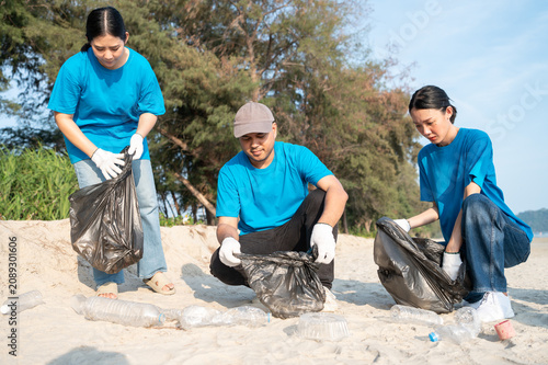 Group of active Asian volunteers cleaning up plastic waste and garbage on the beach together, focusing on environmental conservation and community teamwork.