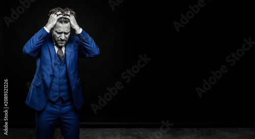 Man in blue suit clutching head showing stress and overwhelm