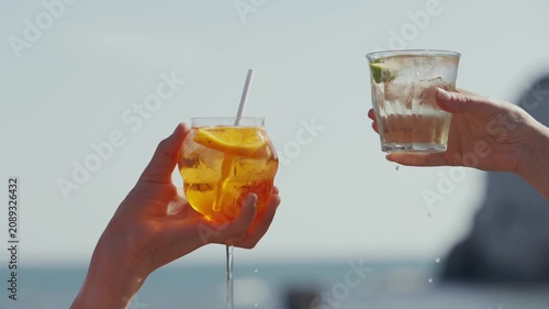 Two hands clink glasses with drinks on a sunny beach vacation