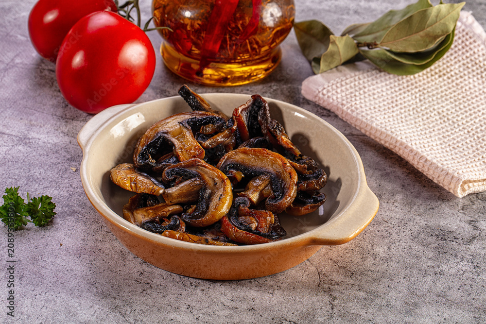 Fototapeta premium Appetizing sauteed mushrooms in a ceramic bowl with fresh ingredients on a stone table