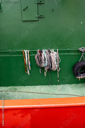 A collection of various ropes and a spare tire hang on the green hull of a boat docked in Zarautz