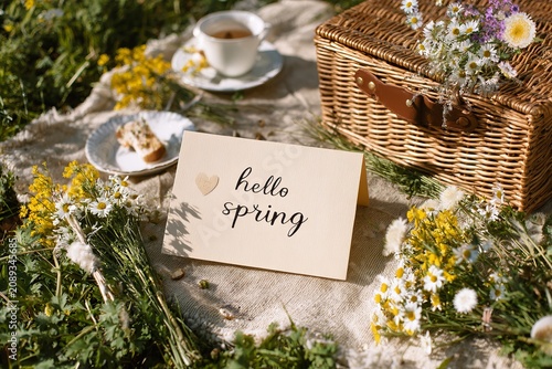 Welcoming spring with a delightful picnic scene adorned with fresh flowers and cheerful messages in a sunny meadow