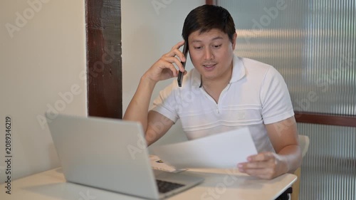 Asian freelancer talking on phone and working on laptop