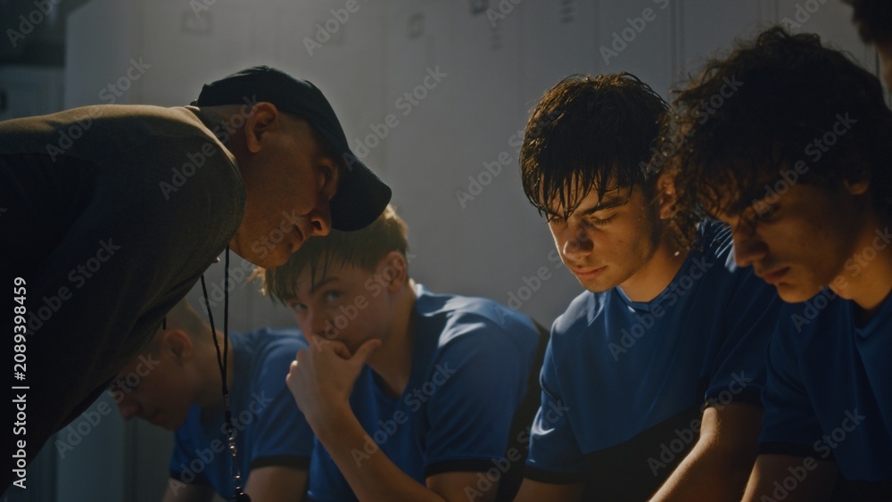 Fototapeta premium Middle Aged Sports Coach Lecturing Youth Soccer Team in Locker Room. Team Sits Quietly on Benches, Processing Harsh Feedback. High Stakes, Tension, and Emotional Weight of Competitive Youth Sports.