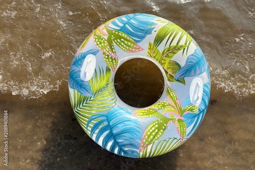 Photography A vibrant, tropical-patterned inflatable swim ring floating on the water near the sandy shore