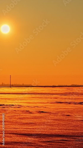 Winter sunset over snow covered fields beneath glowing orange sky, vertical backdrop, drone orbit over twinkling landscape