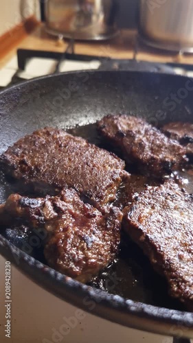 Dark meat patties sizzle and fry in hot bubbling oil inside a rustic cast iron skillet. Concept of home cooking, savory comfort food, and traditional daily protein preparation.