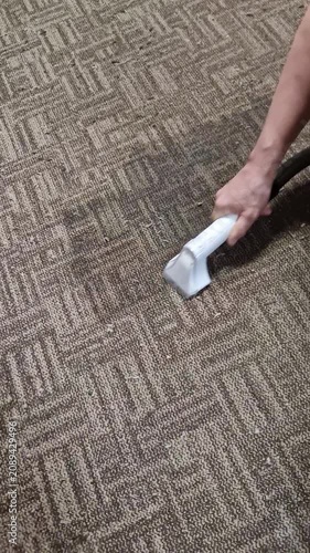 A hand uses a transparent wet vacuum nozzle to extract a dark stain from a textured brown carpet. Concept of deep cleaning, professional home maintenance, and removing dirt.