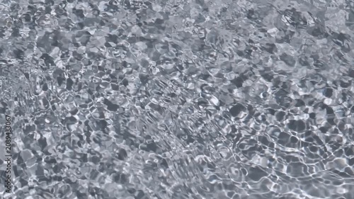Sunlight reflects on the surface of clear rippling water flowing over smooth grey stones. Concept of summer relaxation, pure nature, liquid motion, and refreshing spa atmosphere.