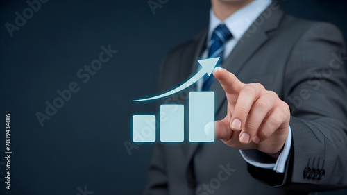 Businessman pointing at growing blue financial bar chart with arrow upward indicating success corporate development profit increase market analytics.