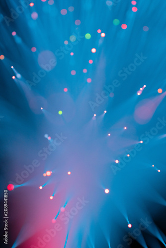 Abstract fiber optic light explosion with colorful bokeh dots on dark teal background
