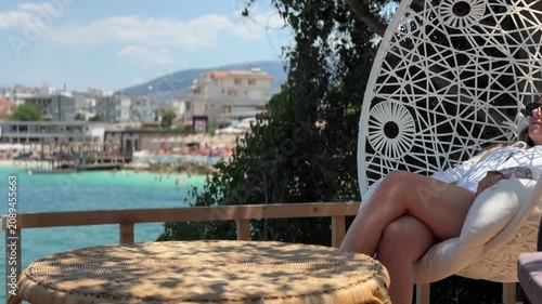 Woman relaxing in hanging chair at beachfront cafe with sea view