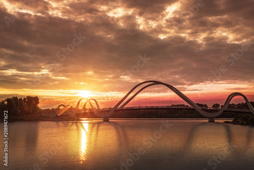 Sunrise over the pedestrian bridge across the Dnipro River in Kyiv, Ukraine. Golden sunlight breaks through pink clouds, reflects on calm water, and slowly rises above the city skyline.