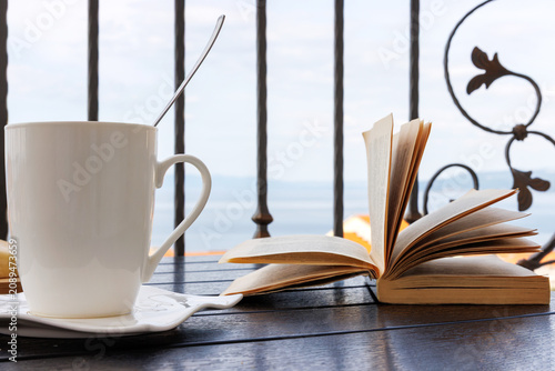 Photos White coffee cup and open book on a balcony table overlooking the Adriatic Sea in Makarska, Croatia