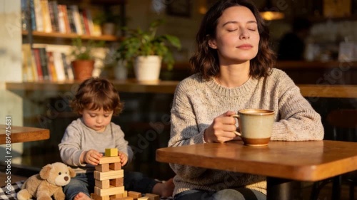 A peaceful mother enjoys a quiet coffee moment while her young child plays with wooden blocks, capturing family life, mindfulness, and everyday parenting.