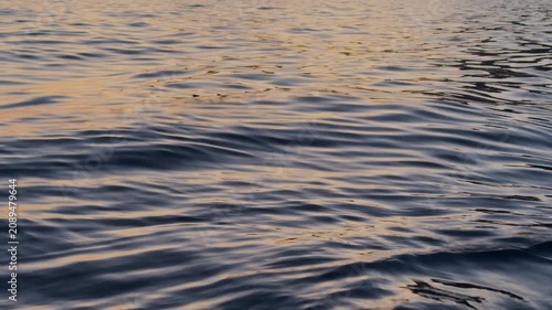 Dark ocean surface shimmering with warm golden reflections of the setting sun, waves and glowing evening light