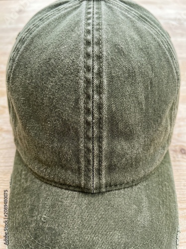 Close up of an olive green washed cotton baseball cap with distressed texture on a light wooden background, casual vintage fashion concept.