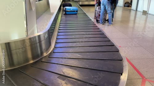 Blue suitcase on conveyor belt, airport arrival carousel with spinning rubber flaps and stainless steel rim, glossy polycarbonate