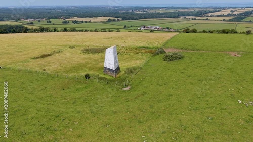 Ashey Down Sea Mark obelisk seen on a slow right ascending drone orbit above open farmland, a historic maritime navigation seamark on the Isle of Wight, England.
