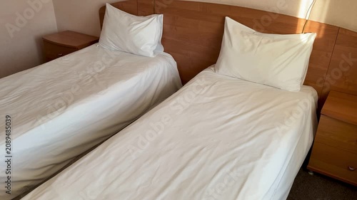 Closeup economy twin beds wrinkled linen. Neutral room with wooden headboard, nightstand and carpet crisp white sheets