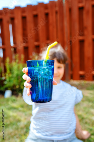 Child girl extending a blue cup toward the camera in a backyard garden