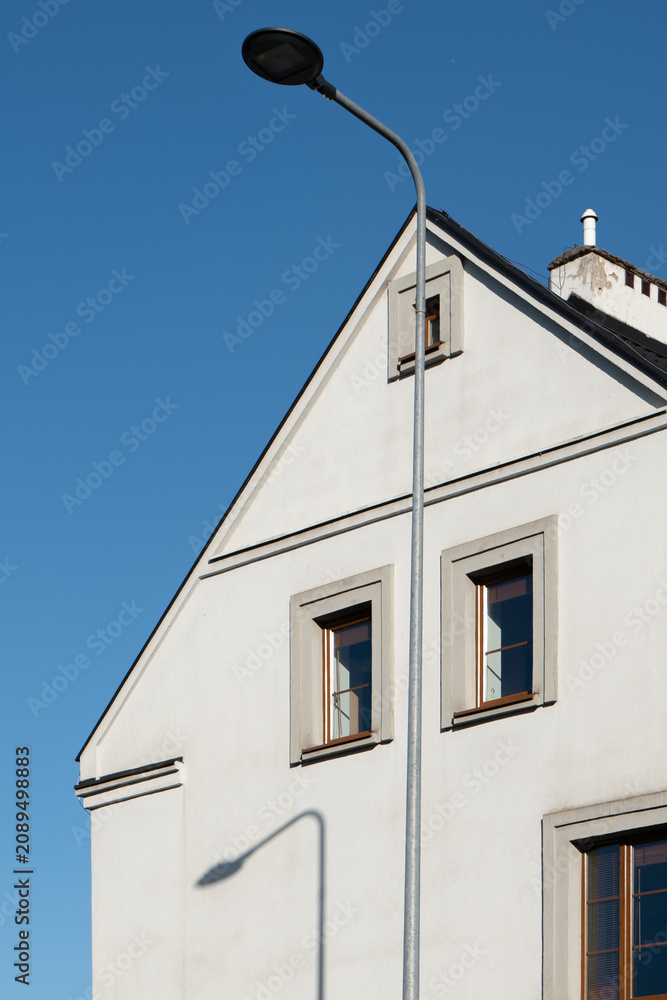 Obraz premium Street light pole casting a shadow on a white residential house facade