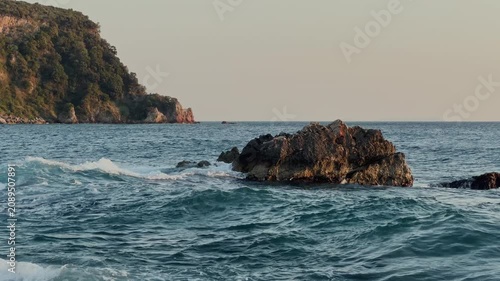 Sea waves crashing against coastal rocks at sunset, with towering cliffs in the background