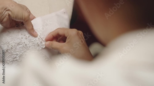 Hand stitching pearl embellished lace onto bridal dress during couture production