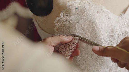 Precision trimming lace edge on custom bridal gown during couture finishing