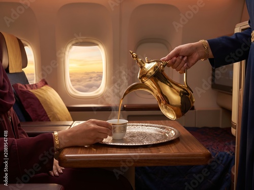 Flight attendant pouring traditional Arabic coffee for passenger in luxury airplane cabin at sunset