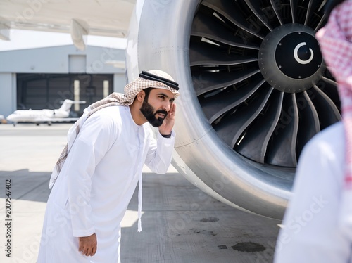 Arab businessman in traditional attire inspecting a large aircraft jet engine at a private hangar