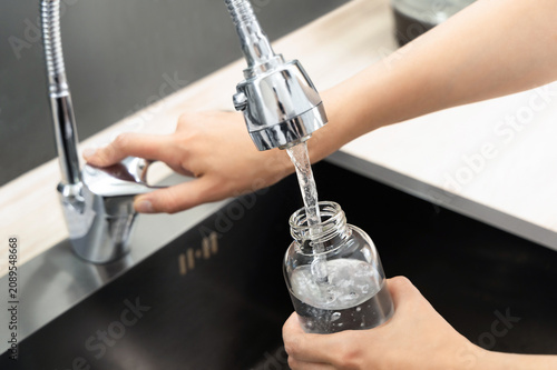Close-up of a woman filling a glass bottle with tap water. Reusable and Less Plastic concept.