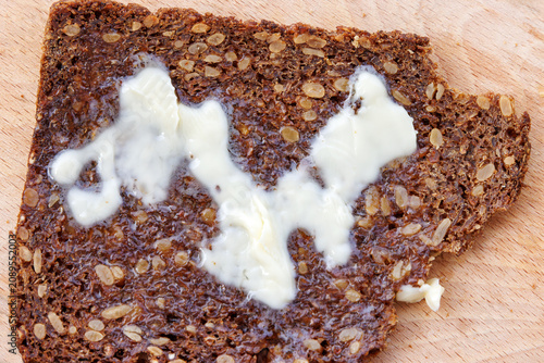 Foto Closeup of a textured slice of sourdough wholegrain rye bread with nuts and grains, topped with melting butter, on a wooden board