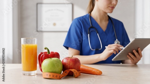 Nutritionist using digital tablet next to fresh fruits and vegetables for healthy diet planning in a bright medical office setting for patient care