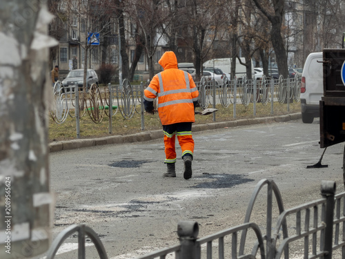A construction worker in high visibility gear repairs road potholes with a shovel on a busy city street to ensure essential infrastructure maintenance during the bright daylight