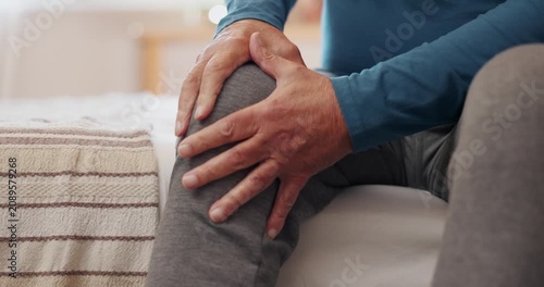 Senior adult sitting on a sofa holding a painful knee due to arthritis, joint inflammation, or injury. Concept of knee pain, aging, orthopedic disorders, rehabilitation, and healthcare.